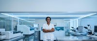 African American female scientist standing confidently in modern laboratory with arms crossed wearing white lab coat surrounded by advanced equipment.