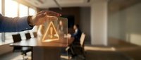 Professional businessman pointing at glowing warning triangle symbol in modern office conference room for business risk management and alert concepts.