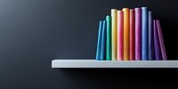 Colorful books arranged in rainbow spectrum order standing on white shelf against dark background, creating minimalist composition with copy space.