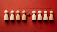 Wooden peg dolls arranged in two rows with arrow showing movement or transition on vibrant red background. Concept of team reorganization.
