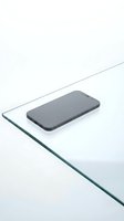 Modern black smartphone placed on transparent glass surface with clean white background for minimalist technology design concepts.