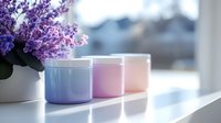 Pastel colored ceramic containers on white windowsill with purple lilac flowers in soft morning light creating serene minimalist home decor composition.