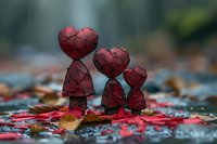 Red heart-shaped figures arranged in descending size on autumn leaves and wet surface, creating emotional family scene with artistic bokeh background effect.