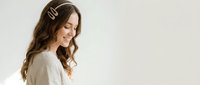 Young woman with long wavy brown hair wearing white shirt and hair clips, smiling in profile against neutral background for lifestyle content.