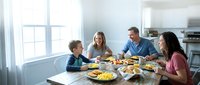 Happy family of four enjoying breakfast together at modern kitchen table with natural sunlight streaming through windows.