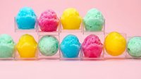 Colorful bath bombs in clear containers arranged on pink background. Isolated product display featuring turquoise, pink, yellow, and green fizzy spheres for spa and wellness marketing.
