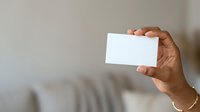 Close-up of a man's hand holding a blank white business card or paper against a neutral beige background, suitable for branding and marketing mockups.