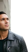 Thoughtful young man with dark hair and olive complexion wearing black leather jacket gazes upward against white wall background, conveying contemplation and introspection for lifestyle and portrait use.