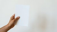 Hand holding blank white paper sheet against neutral background for mockup and branding presentations.
