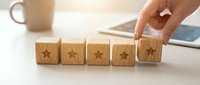 Hand placing wooden cube with star symbol completing five-star rating system on desk for customer feedback and quality assessment in business environment.