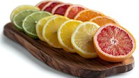 Fresh citrus fruit slices arranged in rainbow gradient on wooden cutting board, including lime, lemon, orange and pink grapefruit, food photography on white background.