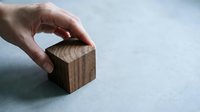 Hand placing wooden cube block on neutral surface for business strategy and building concepts in minimalist setting.