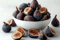Fresh ripe purple figs in ceramic bowl and cut in half showing juicy red flesh on white background, ready for healthy eating or gourmet cooking.