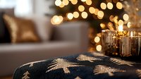 Cozy winter evening atmosphere with knitted Christmas tree pattern on dark blue sweater, blurred golden bokeh lights and candles in background.