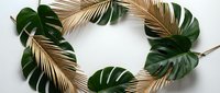 Tropical wreath with golden palm fronds and green monstera leaves on white background. Natural botanical decoration for summer events and interior design.
