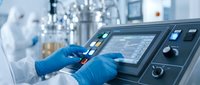 Laboratory technician in protective suit operating digital control panel in sterile pharmaceutical manufacturing facility for quality control testing.