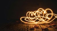 Glowing light painting hearts on rustic wooden surface with rose petals, warm golden bokeh trails on dark background, romantic Valentine concept.