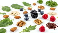 Healthy superfood collection with fresh berries, nuts, seeds and leafy greens on white background for nutrition and wellness concepts.