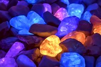 Glowing mineral stones in vibrant neon colors - purple, blue, orange and pink crystals illuminated from beneath creating magical mystical atmosphere.