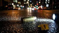 Crime scene investigation with bullet casing and evidence marker on wet asphalt street at night with police car lights and urban traffic bokeh background.
