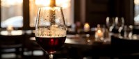 Elegant red wine glass with rich burgundy wine in upscale restaurant setting with warm ambient lighting and blurred dining background for hospitality concepts.