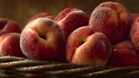 Fresh ripe peaches with water droplets in rustic woven basket against dark background, highlighting natural texture and juicy appearance.