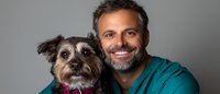 Happy middle-aged Caucasian male veterinarian in teal scrubs smiling with small mixed breed dog patient. Professional pet healthcare and animal medicine concept.