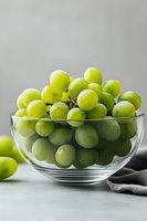 Fresh green grapes in transparent glass bowl on light background with gray textile napkin. Clean food photography for menu, cookbook or blog.