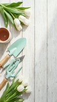 White tulips and mint green gardening tools arranged on rustic wooden background with copy space for spring gardening and planting projects.