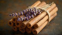 Aromatic bundle of cinnamon sticks tied with twine and decorated with fresh purple lavender flowers on rustic dark background, creating cozy atmosphere.