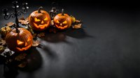 Spooky Halloween jack-o-lantern pumpkins with glowing candles on dark background with autumn leaves and decorative elements for seasonal holiday celebrations.