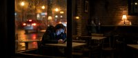 Man working late at night in office with rainy window, urban cityscape lights blurred in background, warm desk lamp illuminating workspace for overtime work.
