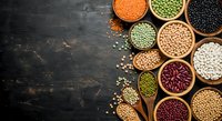 Assorted legumes and beans in wooden bowls on dark rustic background. Healthy protein sources including lentils, chickpeas, kidney beans for cooking.