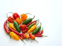 Assorted fresh chili peppers in red, yellow, and green varieties arranged on white background, ready for cooking, culinary design, and food photography projects.
