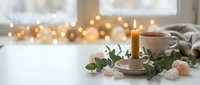 Cozy home interior with burning candle, eucalyptus leaves, rose quartz crystals and warm fairy lights creating peaceful hygge atmosphere for relaxation.