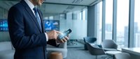 Professional businessman in dark suit using smartphone in modern office with large windows and city view for corporate communication and business technology.