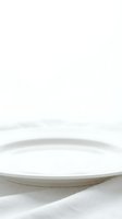 Empty white ceramic plate on neutral fabric surface with soft natural lighting for product display and tableware presentation.