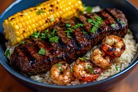 Grilled steak and shrimp surf and turf served on white rice with roasted corn on cob garnished with fresh herbs, close up view of gourmet dinner plate.