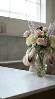 Woman arranging fresh spring flowers in glass vase on marble kitchen counter. Elegant home decor and floral design concept for interior styling.