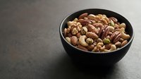 Mixed nuts and dried fruits in black bowl on dark surface for healthy snacking and cooking ingredients.