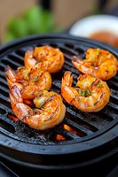 Grilled jumbo shrimp with herbs and spices on cast iron grill pan, close up view showing caramelized glaze and char marks. Fresh seafood cooking process.