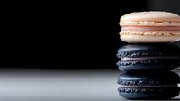 Stack of colorful macarons with pink and dark blue flavors on black background, French pastry dessert for bakery menu and culinary photography.