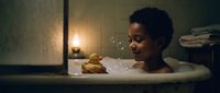Young African American woman relaxing in bathtub with rubber duck toy and soap bubbles in cozy bathroom setting with warm candlelight atmosphere.