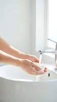Woman washing hands with soap under running water at modern bathroom sink for hygiene and cleanliness routine.