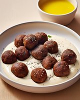 Homemade meatballs served on creamy sauce with black sesame seeds, accompanied by yellow soup in ceramic bowl on wooden table.