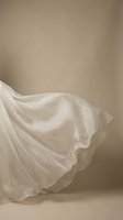 Flowing white silk fabric with elegant drape and soft folds against neutral beige background for luxury fashion and textile design projects.