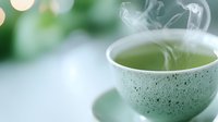 Steaming hot green tea in speckled ceramic cup against soft blurred background, with rising vapor creating delicate swirls in morning light.