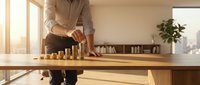 Professional businessman in beige suit stacking golden coins on wooden desk in modern office, representing financial growth and investment success.