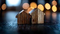 Wooden house shapes on dark surface with blurred golden bokeh lights in background creating cozy atmosphere. Concept of real estate, home ownership and family.