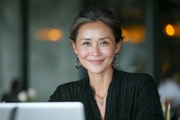Confident mature Asian businesswoman smiling at camera in cafe setting, showcasing professional success and approachability.
